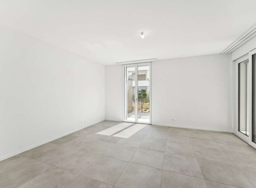 Experience modern living in this bright and airy empty room, featuring sleek tiled flooring and expansive glass doors that open to a serene outdoor space.