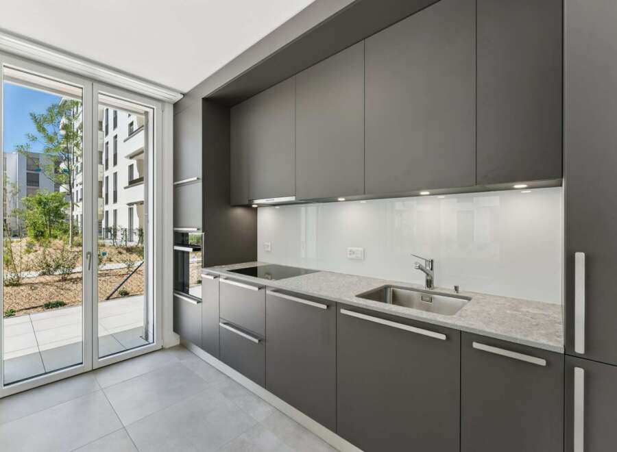 Experience modern living in this sleek, contemporary kitchen featuring dark gray cabinetry and a pristine white backsplash.