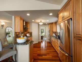 This beautifully remodeled kitchen features warm, natural wood cabinetry and gleaming stainless steel appliances, including a large side-by-side refrigerator.