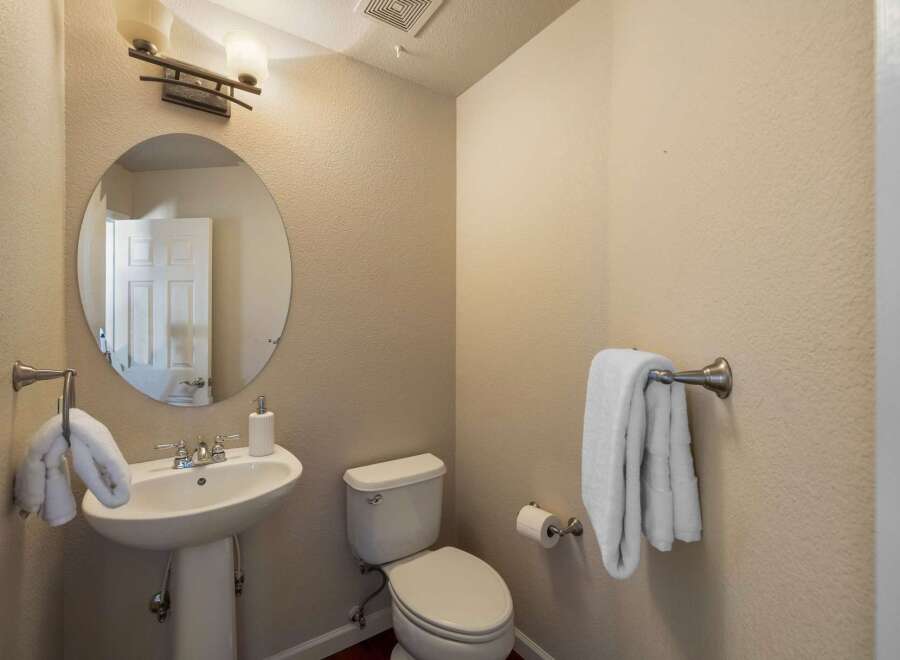 This powder room features a pedestal sink with a chrome faucet and a round mirror above.