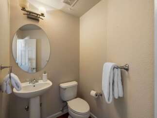 This powder room features a pedestal sink with a chrome faucet and a round mirror above.