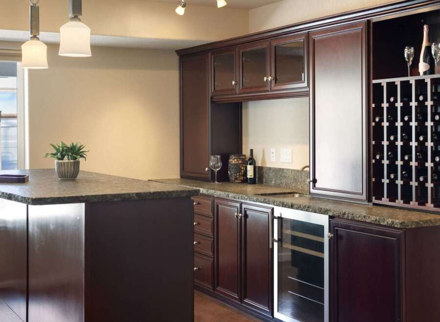 This elegant home bar features rich, dark wood cabinetry with glass-fronted upper cabinets and a built-in wine rack.
