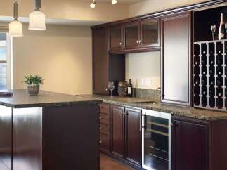 This elegant home bar features rich, dark wood cabinetry with glass-fronted upper cabinets and a built-in wine rack.