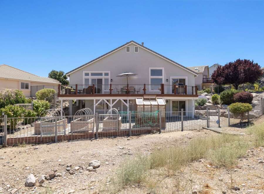 Enjoy outdoor living with a spacious deck overlooking a fenced backyard featuring raised garden beds and a greenhouse.