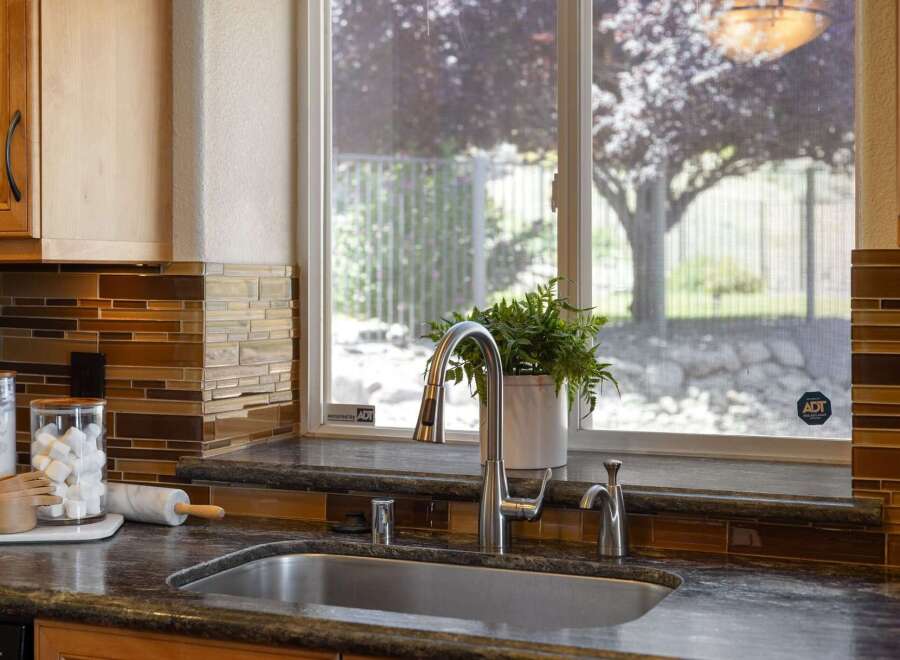 This kitchen features a sleek stainless steel sink and faucet, complemented by a beautiful mosaic tile backsplash in warm brown and amber tones.