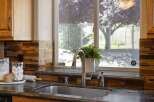 This kitchen features a sleek stainless steel sink and faucet, complemented by a beautiful mosaic tile backsplash in warm brown and amber tones.