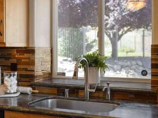 This kitchen features a sleek stainless steel sink and faucet, complemented by a beautiful mosaic tile backsplash in warm brown and amber tones.