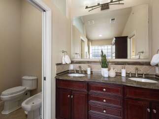 This luxurious bathroom features a spacious double vanity with a granite countertop and rich cherry wood cabinetry, perfect for ample storage.