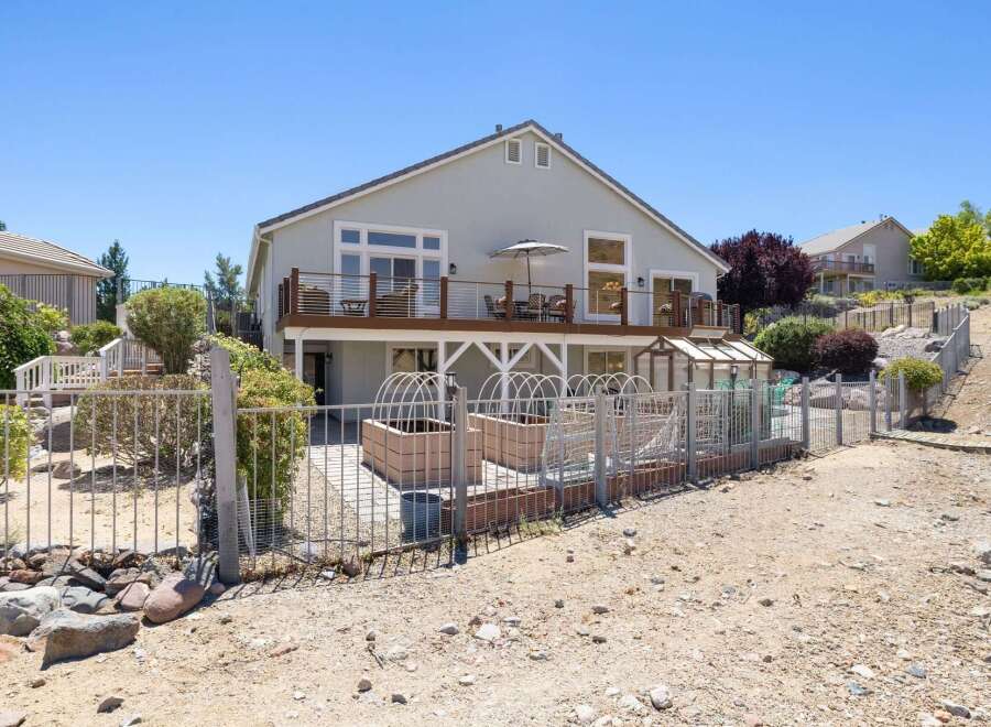 Enjoy outdoor living with this spacious deck overlooking a fenced backyard featuring raised garden beds and a greenhouse.