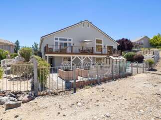 Enjoy outdoor living with this spacious deck overlooking a fenced backyard featuring raised garden beds and a greenhouse.