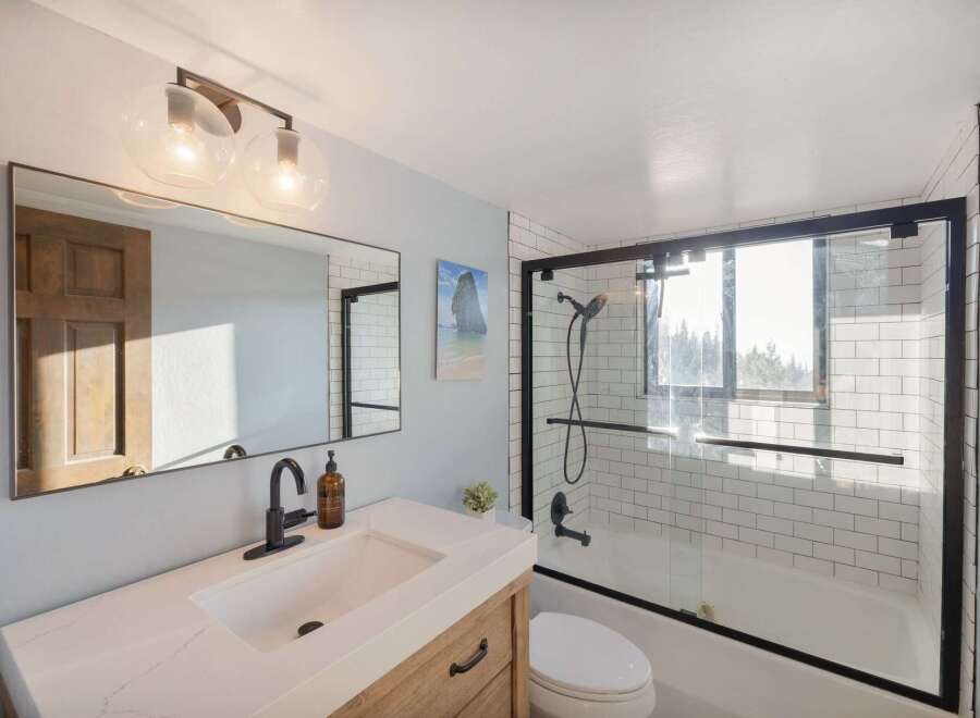 This modern bathroom features a sleek vanity with a quartz countertop and a black faucet, complemented by a large mirror reflecting a wooden door.