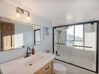 This modern bathroom features a sleek vanity with a quartz countertop and a black faucet, complemented by a large mirror reflecting a wooden door.