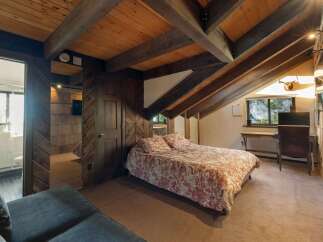 Experience rustic charm in this unique attic bedroom, featuring exposed wooden beams and a cozy bed with a nature-inspired duvet.
