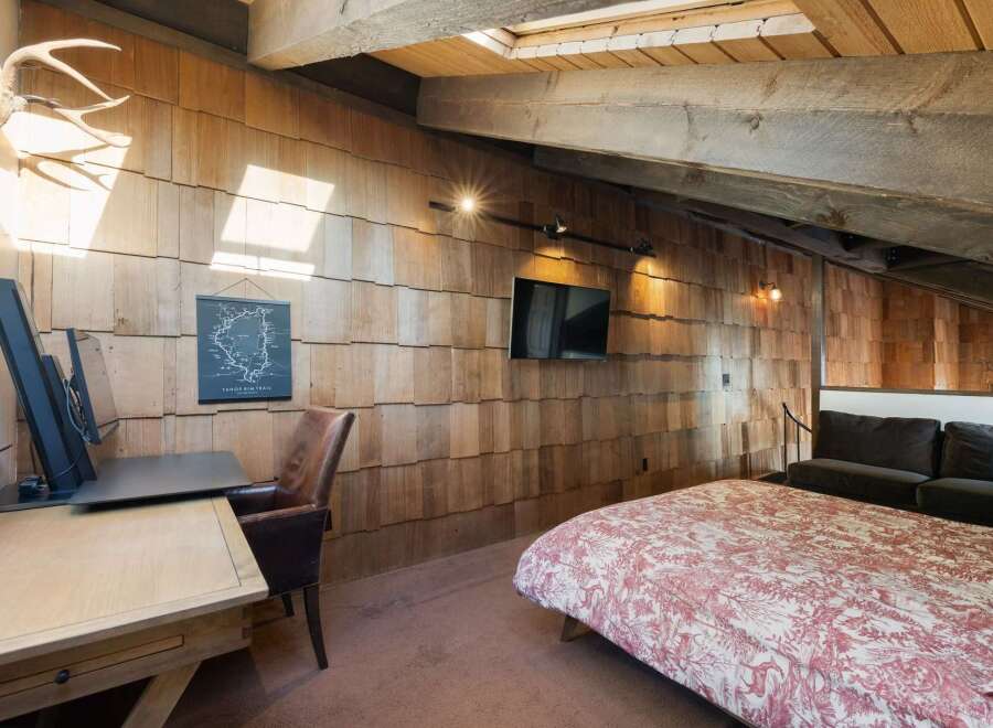 Experience rustic charm in this unique attic bedroom, featuring a striking wood-shingled wall and exposed wooden beams.