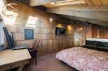 Experience rustic charm in this unique attic bedroom, featuring a striking wood-shingled wall and exposed wooden beams.