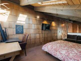 Experience rustic charm in this unique attic bedroom, featuring a striking wood-shingled wall and exposed wooden beams.