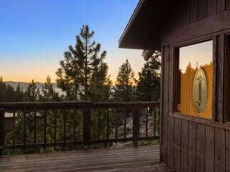 Experience breathtaking sunset views from this charming cabin deck, overlooking a serene lake and majestic mountains.