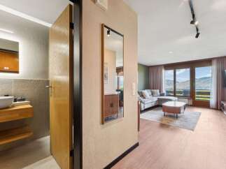 Experience breathtaking mountain views from this stunning apartment, featuring a spacious living area with a comfortable sectional sofa and a modern coffee table.