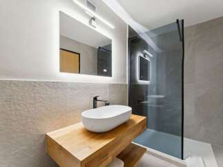 Experience modern luxury in this stunning bathroom featuring a sleek vessel sink atop a warm wooden vanity.