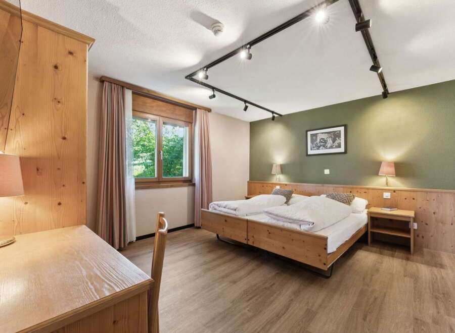 Experience rustic charm in this inviting hotel room, featuring a comfortable wooden bed and a functional desk area.