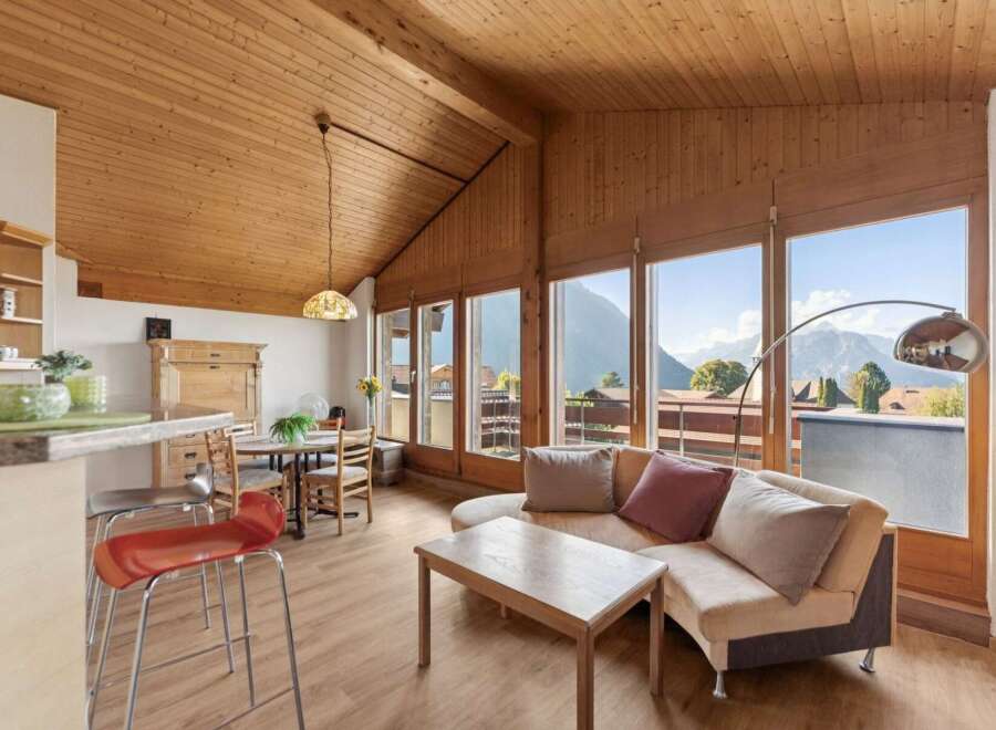 Experience breathtaking mountain views from this charming living space, featuring a vaulted wood-paneled ceiling and expansive windows.