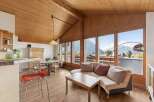 Experience breathtaking mountain views from this charming living space, featuring a vaulted wood-paneled ceiling and expansive windows.