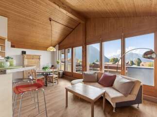 Experience breathtaking mountain views from this charming living space, featuring a vaulted wood-paneled ceiling and expansive windows.