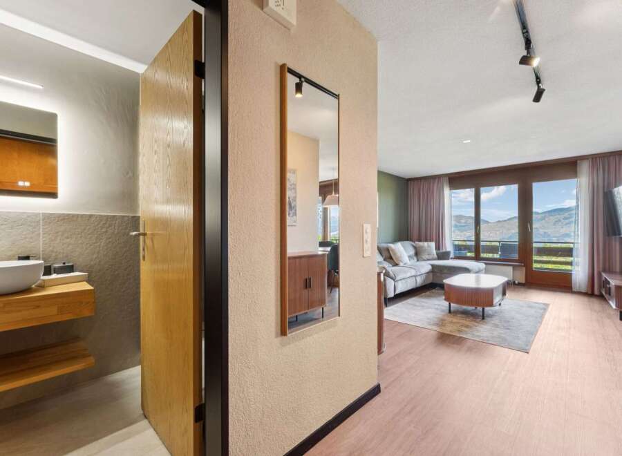 Experience breathtaking mountain views from this stunning apartment, featuring a spacious living area with a comfortable sectional sofa and a modern coffee table.