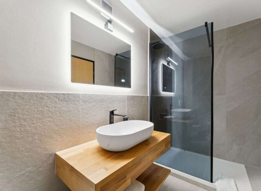 Experience modern luxury in this stunning bathroom featuring a sleek vessel sink atop a warm wooden vanity.