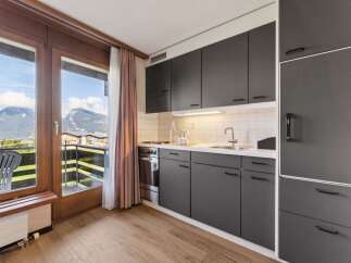 Experience stunning mountain views from this modern kitchen, featuring sleek dark cabinetry and a convenient balcony access.