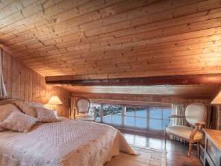 Experience cozy mountain living in this charming attic bedroom, featuring a warm wooden interior and a picturesque view of a snowy landscape through the large windows.