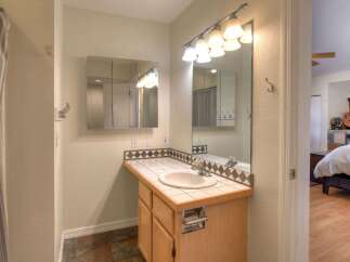 This bathroom features a spacious vanity with a tiled countertop and a built-in sink, complemented by a large mirror with an overhead light fixture.