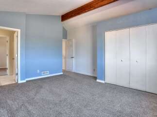Discover comfort and style in this spacious bedroom, featuring calming blue walls and a vaulted ceiling with exposed wooden beams.