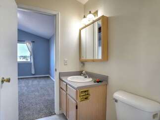 This charming bathroom features a light wood vanity with a gray countertop, complemented by a mirrored medicine cabinet and dual sconce lighting.