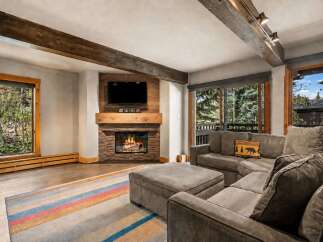 Cozy up by the stone fireplace in this inviting living room, featuring exposed wooden beams and a large sectional sofa perfect for relaxing.