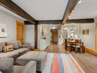 Experience rustic charm in this inviting living and dining area, featuring exposed wooden beams and a cozy sectional sofa perfect for relaxation.