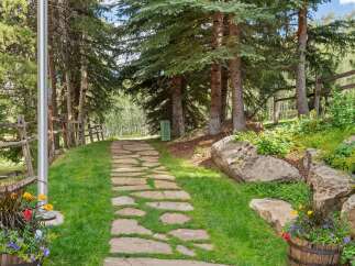 Discover this charming property featuring a picturesque stone pathway winding through lush green grass and mature trees.