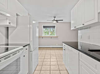 This bright and airy kitchen features white cabinetry and sleek black countertops, offering ample storage and workspace.