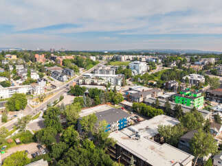 Discover this vibrant urban neighborhood featuring a mix of modern apartment buildings and charming single-family homes, all nestled amongst lush greenery.