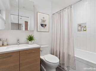 This modern bathroom features a sleek vanity with ample storage, a clean white toilet, and a bathtub with a neutral-toned shower curtain.