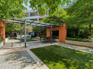 Enjoy outdoor living in this modern courtyard featuring a sleek glass-covered pergola with a dining set, perfect for al fresco meals.