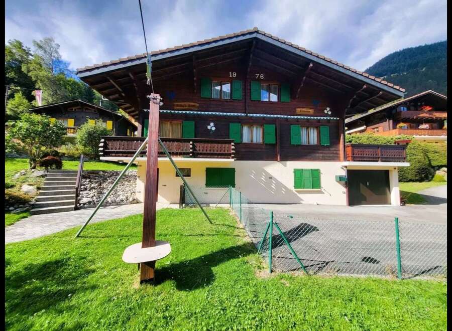 Charming wooden chalet nestled in a picturesque mountain setting, featuring traditional Swiss architecture with vibrant green shutters and a spacious balcony.