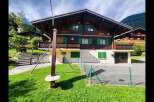 Charming wooden chalet nestled in a picturesque mountain setting, featuring traditional Swiss architecture with vibrant green shutters and a spacious balcony.