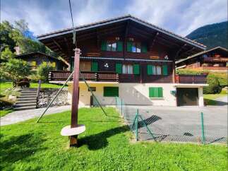 Charming wooden chalet nestled in a picturesque mountain setting, featuring traditional Swiss architecture with vibrant green shutters and a spacious balcony.