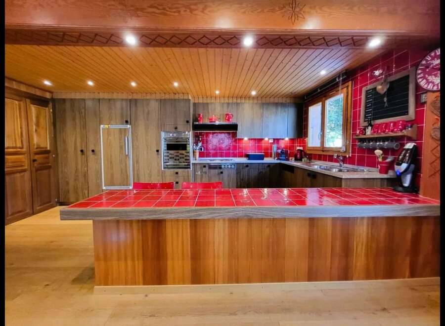 Experience rustic charm in this spacious kitchen featuring warm wooden cabinetry and a vibrant red tiled island countertop.