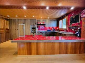 Experience rustic charm in this spacious kitchen featuring warm wooden cabinetry and a vibrant red tiled island countertop.