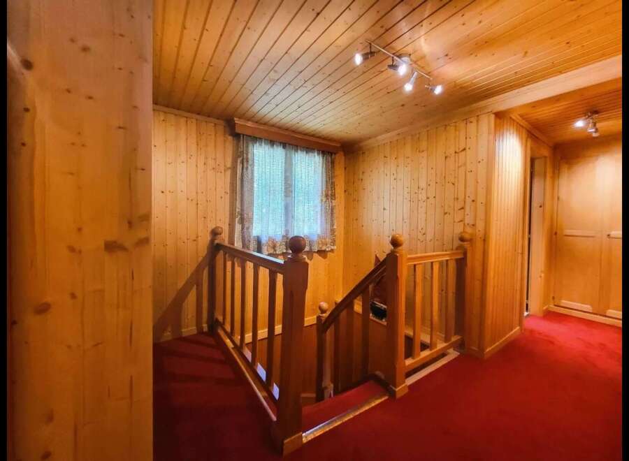Step into a warm and inviting atmosphere with this charming wooden staircase, featuring rich red carpeting for a touch of elegance.