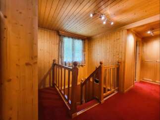Step into a warm and inviting atmosphere with this charming wooden staircase, featuring rich red carpeting for a touch of elegance.