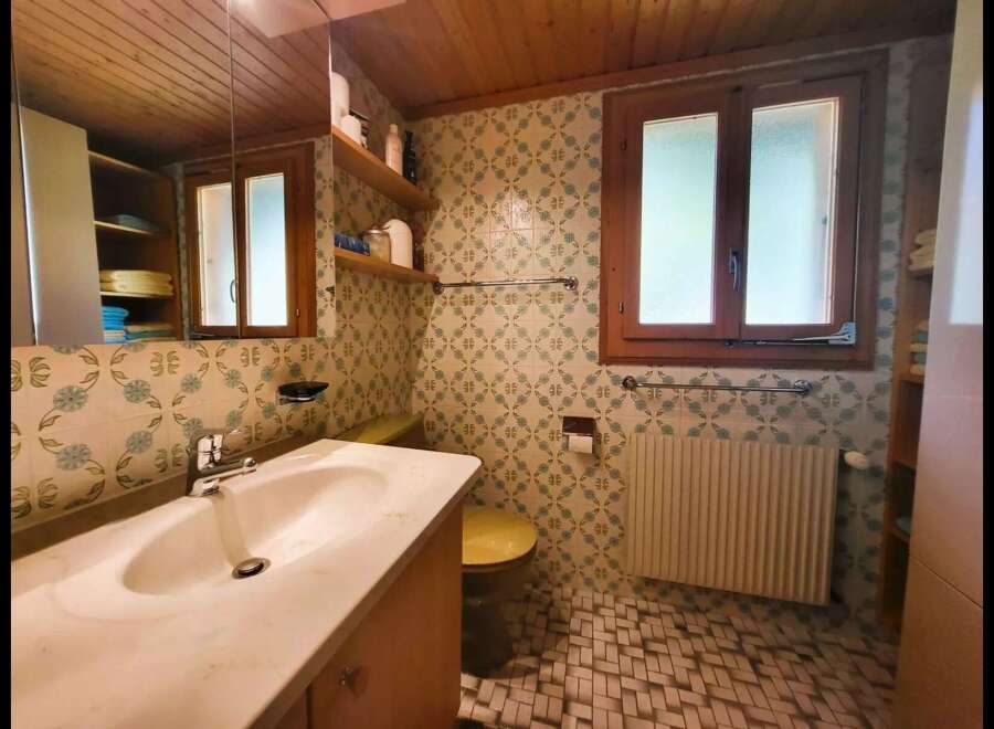 This charming bathroom features a spacious vanity with a marble countertop and a modern faucet, complemented by a large mirror reflecting the wooden ceiling.