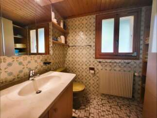 This charming bathroom features a spacious vanity with a marble countertop and a modern faucet, complemented by a large mirror reflecting the wooden ceiling.
